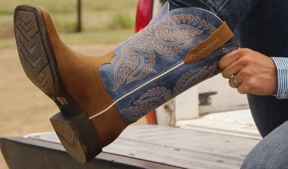 Blue suede cowboy boot with tan leather accents and intricate stitched paisley patterns.