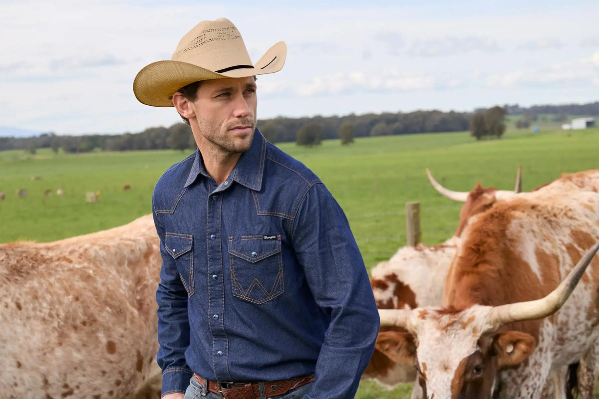 A man wearing a tan cowboy hat and a blue denim shirt with two chest pockets.