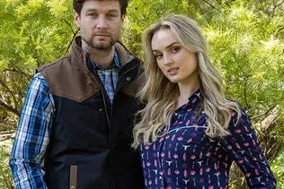 The man wears a brown and black quilted vest over a blue plaid shirt.